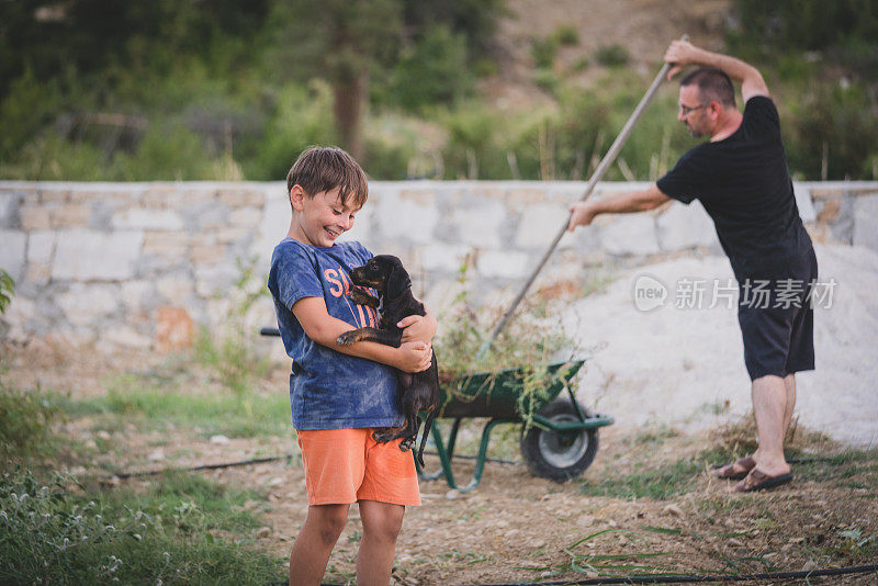 小男孩和他的狗玩，而他的父亲在后院工作