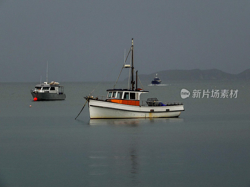 小船停泊在平静的灰色海面上的帕特森湾。拉基拉赛道，斯图尔特岛，新西兰。