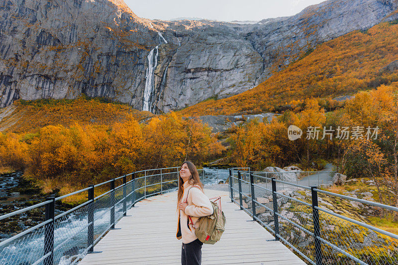 在挪威，女性徒步在风景秀丽的秋谷中欣赏瀑布景观