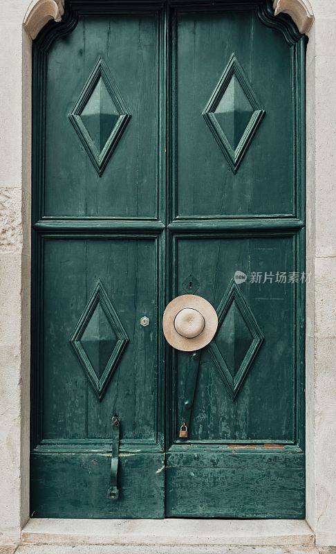垂直拍摄的遮阳帽挂在古老的木制绿色门的门把手上，上面有符号