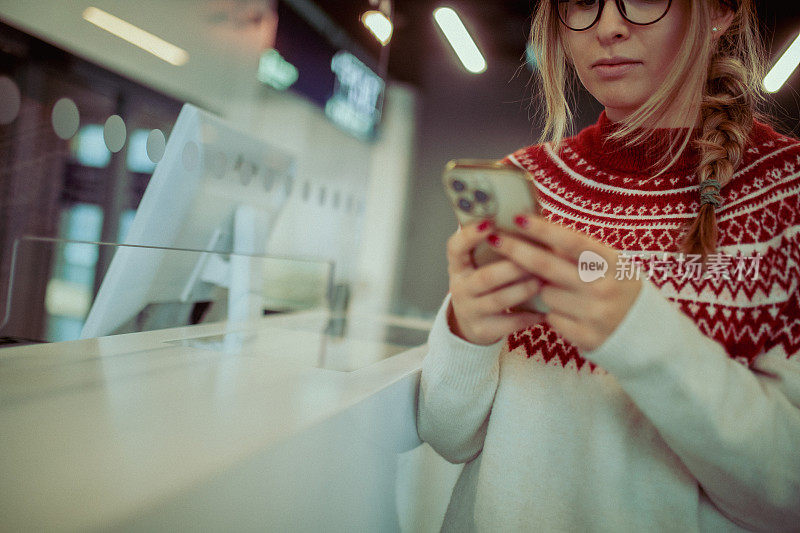 一名女子站在机场柜台前使用手机