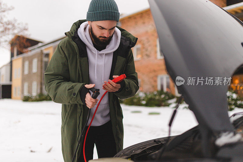 年轻人在冬天用电池电缆启动他的汽车