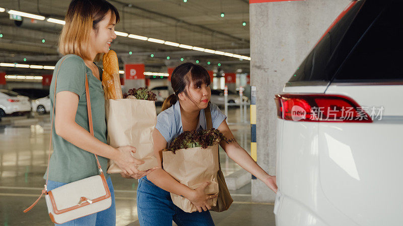 年轻的亚洲女性朋友把装满杂货的购物袋放进停车场的车里。在超市购物。