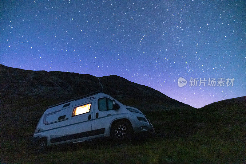 一辆露营车从里面被照亮，站在一个高原上，夜晚繁星点点，没有月亮。