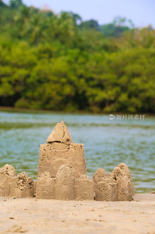 在印度果阿的海滩上建造的复杂沙堡堡垒图像，用桶和铲子制作，并修改为围绕外部创建一堵墙，背景是大海，垂直距离图像