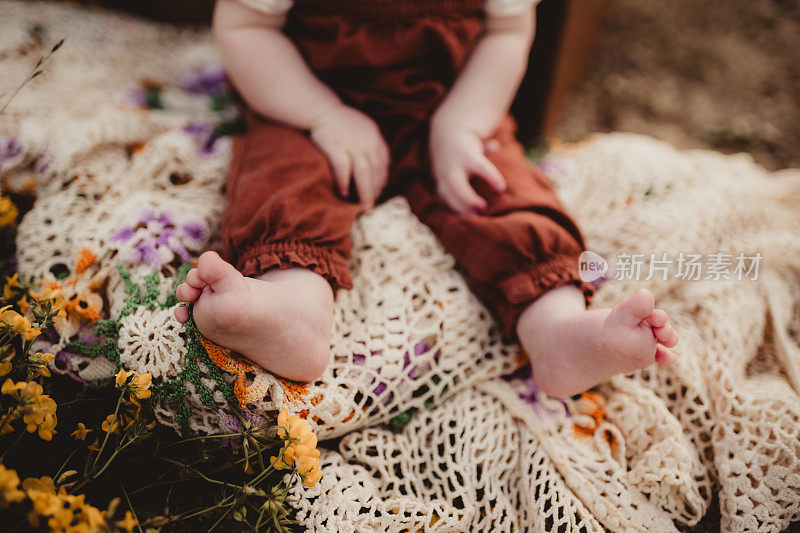 孩子坐在花边钩针编织的毯子上，脚趾伸出来