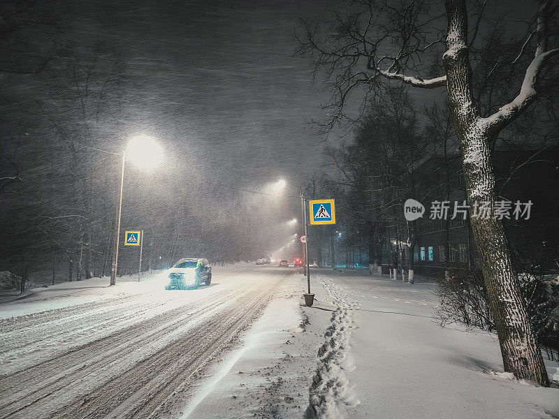 城市街道上的夜雪。一场强烈的暴风雪在高速公路上，郊区的高速公路在灯笼的灯光下，罕见的汽车在雪中缓慢行驶。