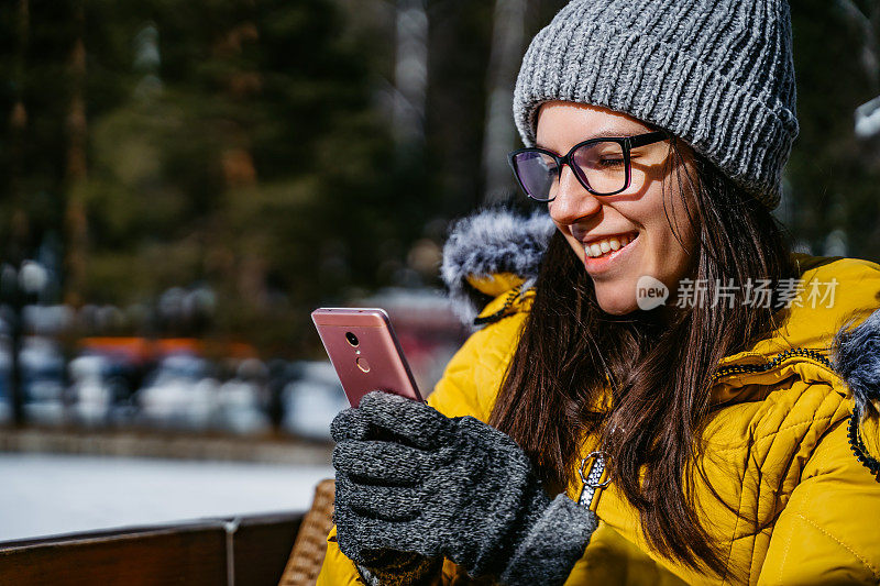 在阳光明媚的冬日里，一名女子在滑雪咖啡馆里使用手机