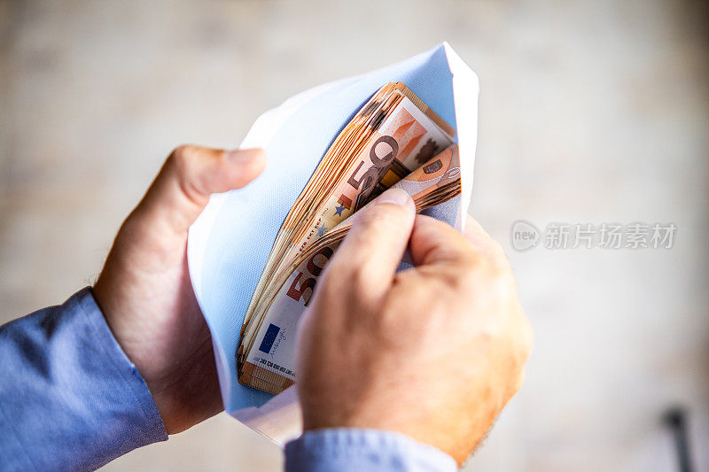 一名男子手里拿着一个信封，里面装着欧元钞票，这是欺诈来源，黑钱或B付款。观点。观点