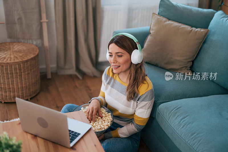 女人坐在家里的地板上放松，开心地吃着爆米花，看着搞笑的电视剧