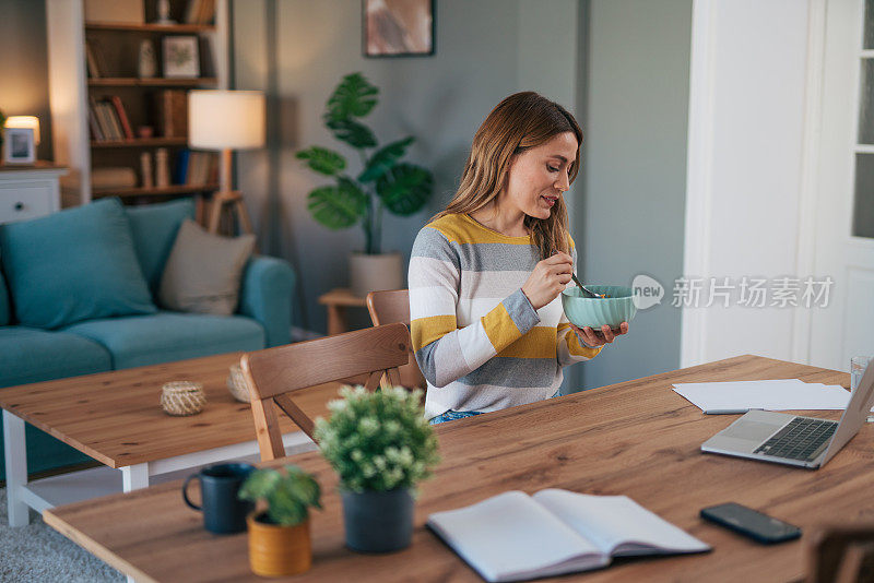 一个成熟的女人一边吃早餐一边用笔记本电脑工作。