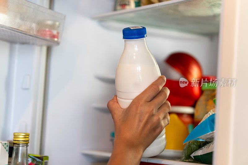 一个孩子的手从冰箱里拿出一瓶酸奶。把牛奶放进冰箱