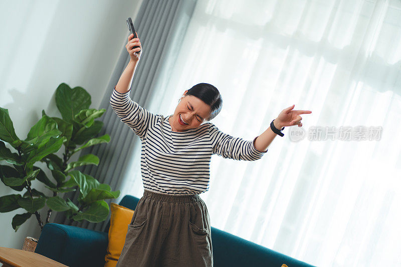 快乐的女人在家里用智能手机和耳机听音乐。