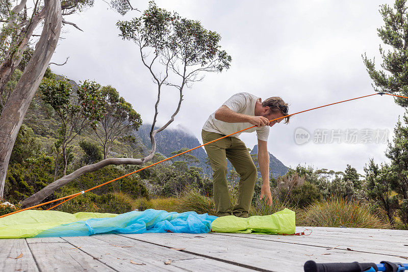 荒野静修:在塔斯马尼亚宁静的风景中，一名男子在木平台上搭帐篷