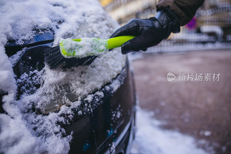 年轻人正在清除汽车前灯上的雪