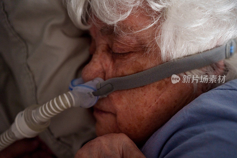 有睡眠呼吸暂停的80多岁高龄妇女在床上睡着，戴着CPAP(持续气道正压通气)机帮助她入睡