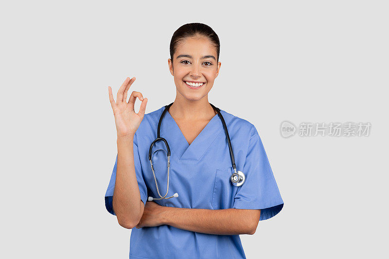 阳性的白人千禧一代女医生或护士穿着蓝色制服，用手表示ok