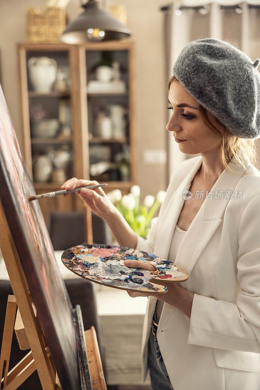 美丽的女画家在家庭美术工作室边画画边享受。女艺术家在艺术工作室从事抽象丙烯绘画。