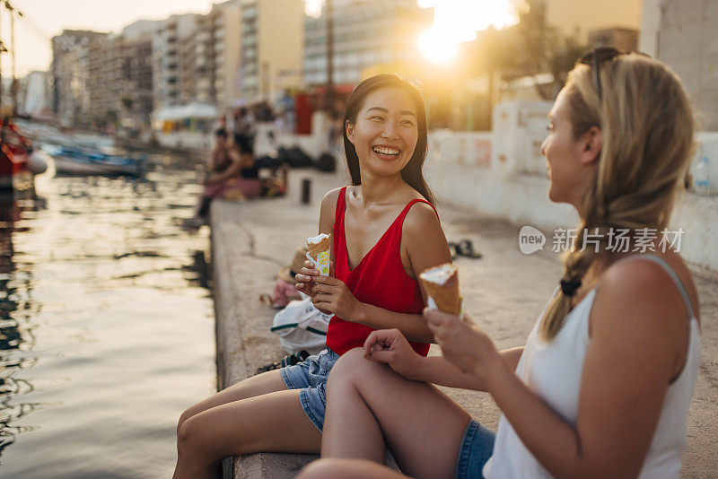 两个朋友坐在码头上享受一个阳光明媚的夏日，吃着甜筒冰淇淋