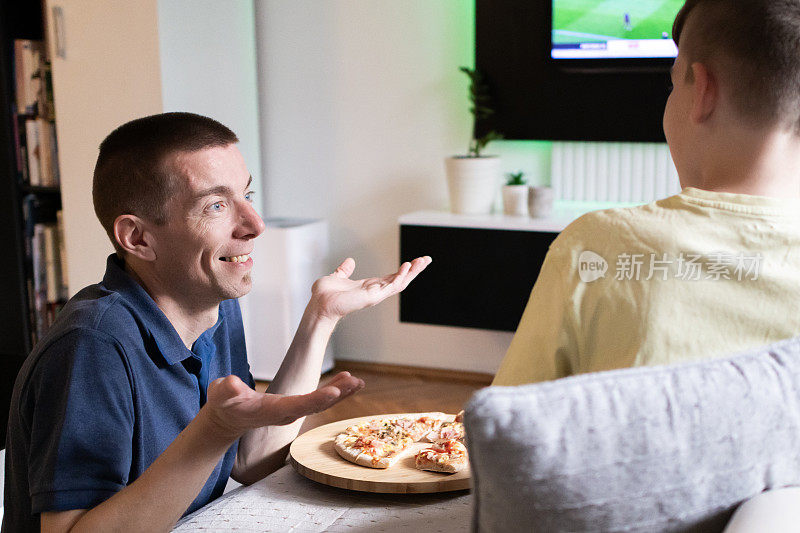 父子俩在一起玩得很开心。他们正在家里吃披萨，看他们最喜欢的足球队的电视转播。