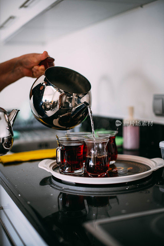 在厨房里，妇女从土耳其传统的茶壶里倒茶到玻璃杯里。