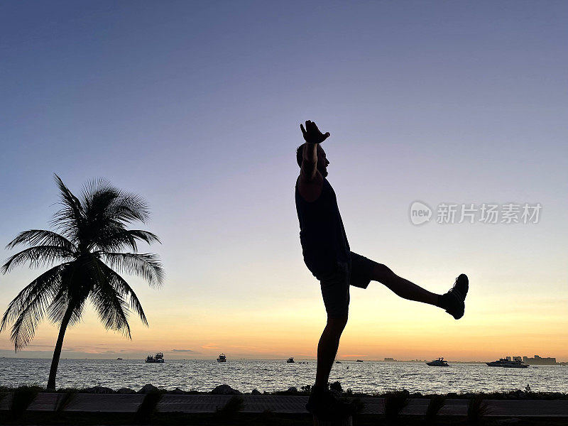 年轻健康的拉丁游客男性旅行在迈阿密和基韦斯特在美国佛罗里达州在夏季炎热的日落日，享受一个自由放松的时间从大海戏剧性的日落金色的天空。