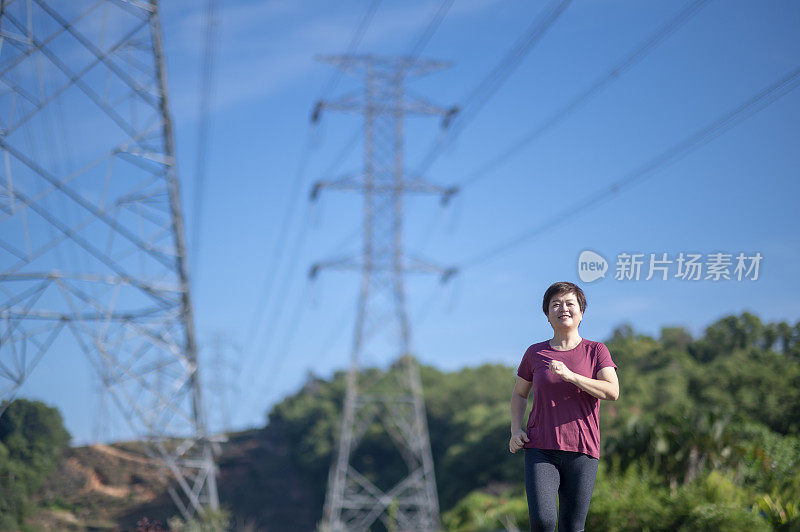 亚洲华人中年妇女与运动服跑步在早上与电力线蓝色的天空背景