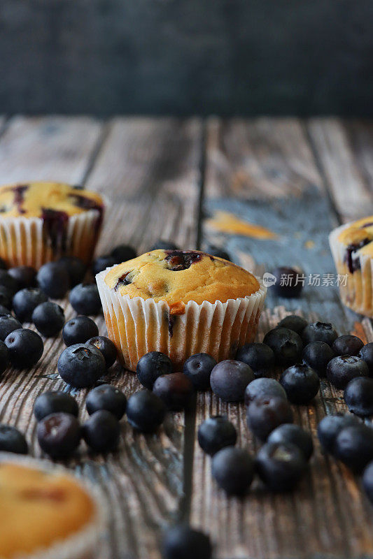 图片批新鲜烘焙的蓝莓松饼在纸蛋糕盒周围的新鲜蓝莓，木纹背景