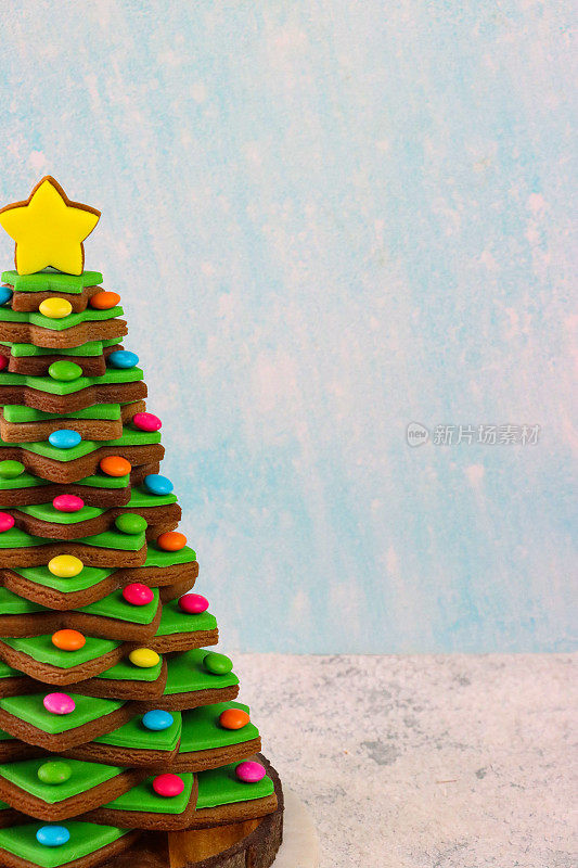 近距离拍摄的圣诞树上堆放着绿色方糖糖霜的姜饼星饼干，装饰着彩色的巧克力糖衣，顶部是黄色的冰星饼干，放在木制蛋糕架上，浅蓝色的雪背景，复制空间