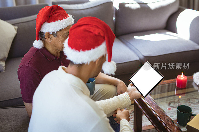 两个种族的成年儿子和年长的父亲戴着圣诞帽在用平板电脑进行圣诞视频通话