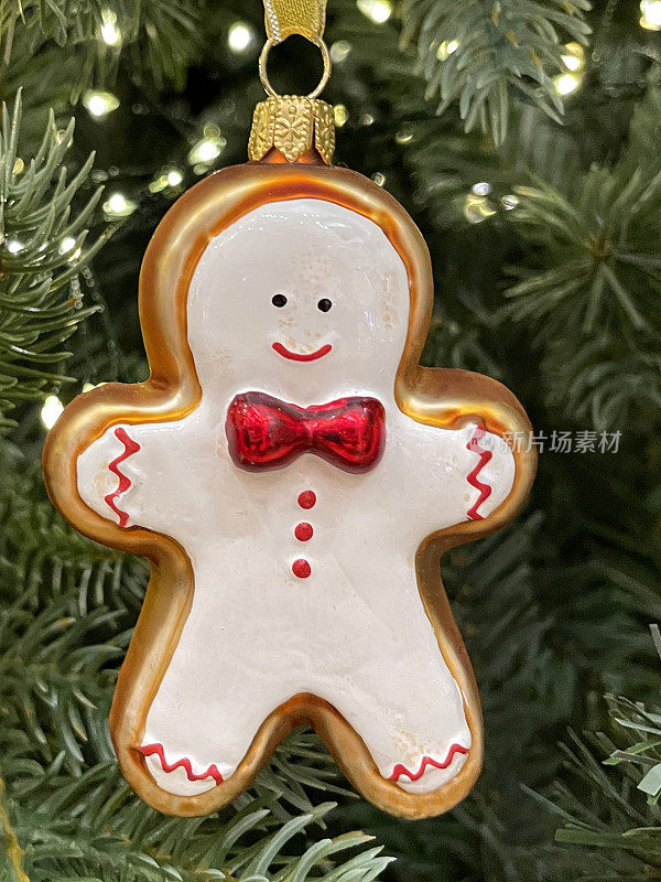 特写图像的姜饼人装饰红色蝴蝶结装饰，在人造圣诞树树枝，云杉针，模糊的白色精灵灯的背景