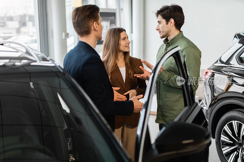 快乐的年轻夫妇在汽车经销店与汽车销售员讨论购买新车