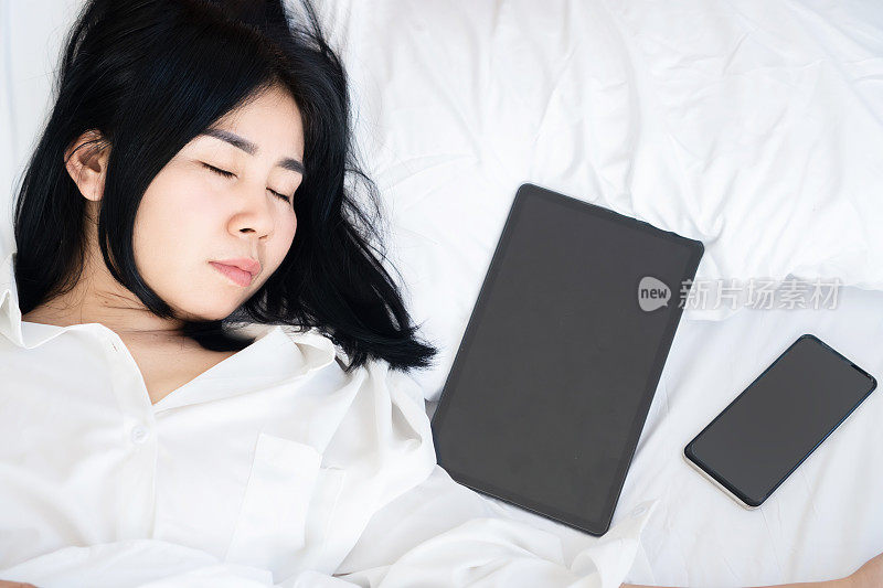 亚洲女性沉迷于科技，在床上睡手机和平板电脑，过度使用互联网，无手机恐惧症的概念