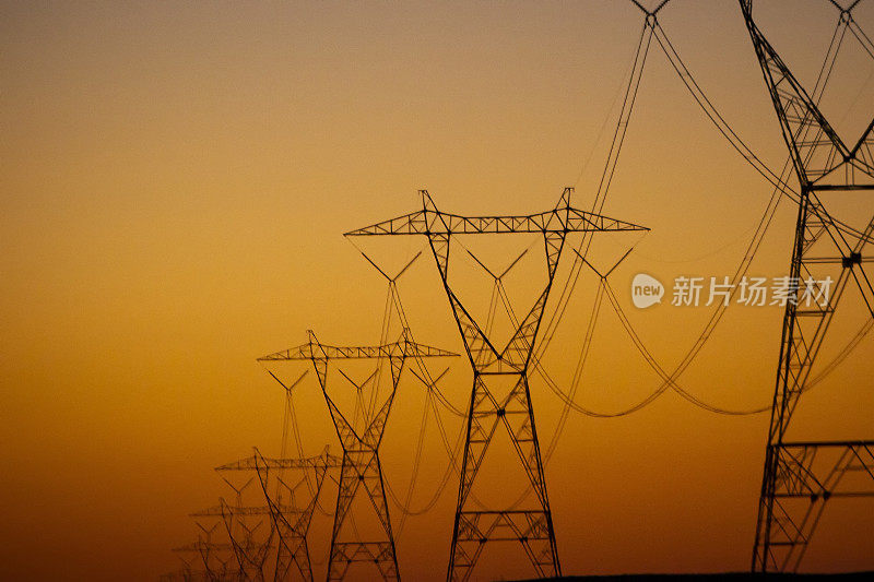 在西南沙漠，一排输电塔的剪影映衬着橙色的夕阳天空