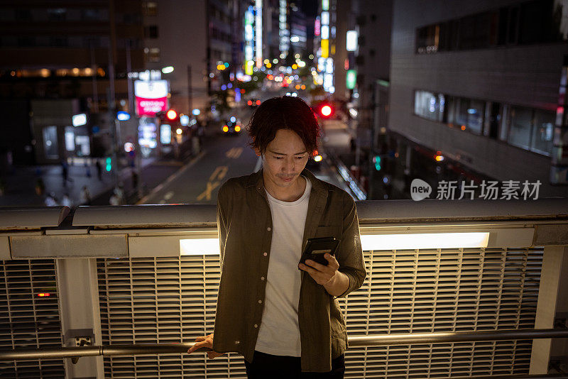 日本男子晚上在人行天桥上使用智能手机