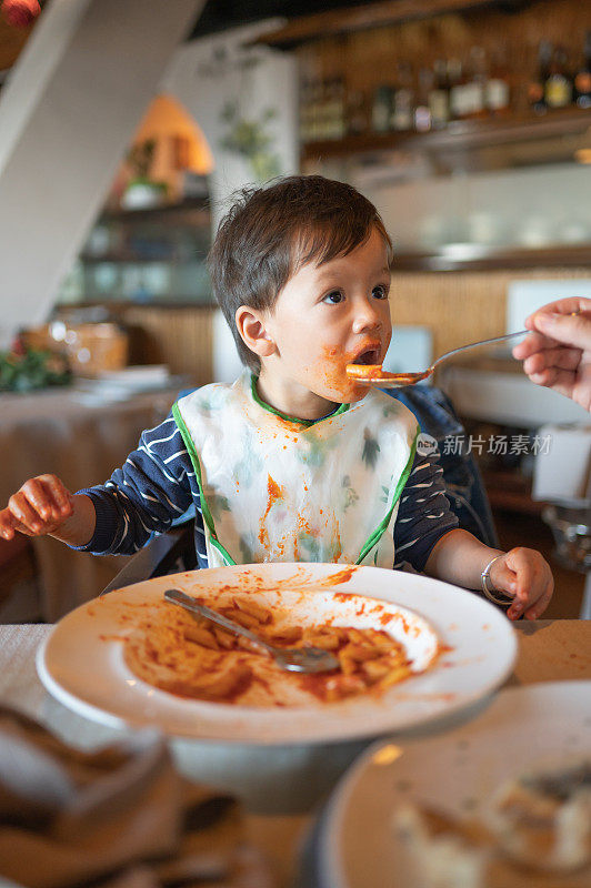 可爱的蹒跚学步的孩子吃意大利面，把自己弄得非常脏，并享受它