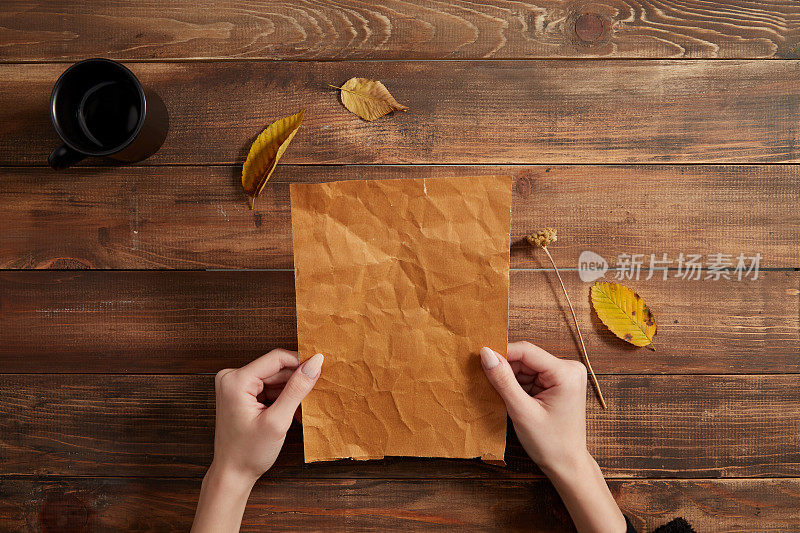 双手拿着一张白纸。木制背景与一杯咖啡和秋叶。