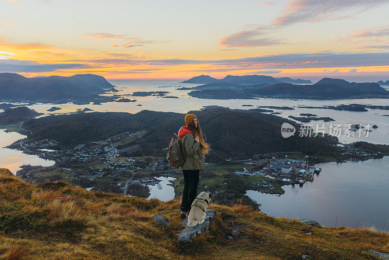 在挪威，一个女人和一只狗在岛屿和大海的顶端凝视日落
