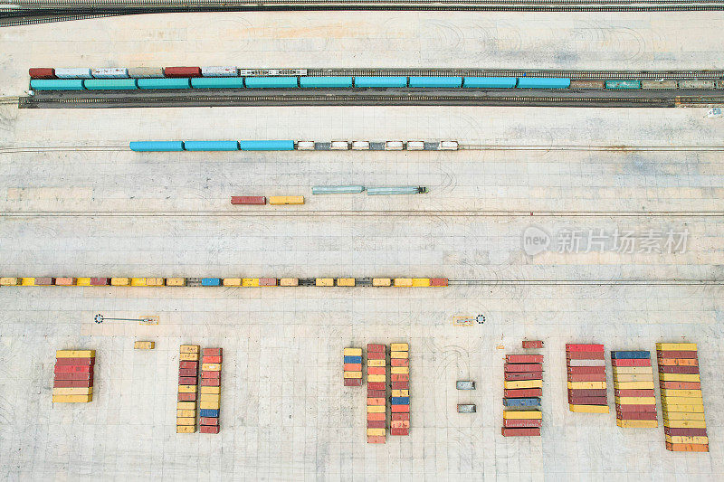 无人机视角下，物流中心的运输集装箱排成一排，火车轨道在其一侧