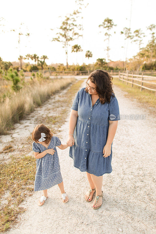 在佛罗里达州的朱庇特农场，一名31岁的妇女牵着她三岁的古巴裔美国人女儿的手，她有棕色卷发和棕色眼睛，穿着蓝色连衣裙和凉鞋