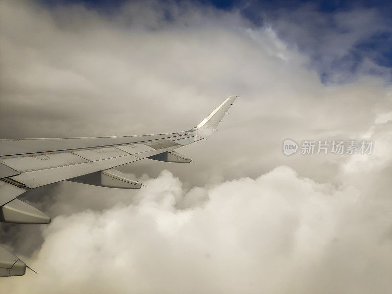 从飞机机翼的窗户看，在云层和蓝天上飞行。