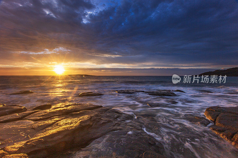 长时间曝光的海水在岩石上流动的海景与戏剧性的金色日落