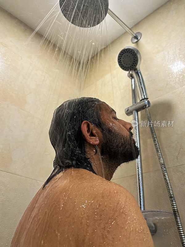 印度男子在淋浴间洗头的特写照片，洗发水泡沫在流水下冲洗掉，抬头看，棕色马赛克瓷砖墙，侧面视图，焦点在前景