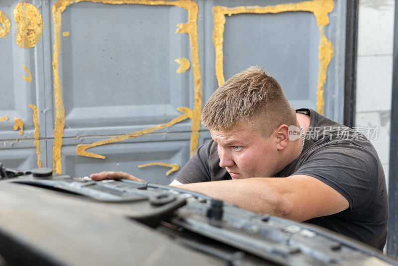 年轻的汽车修理工正在他的车库里修理汽车。