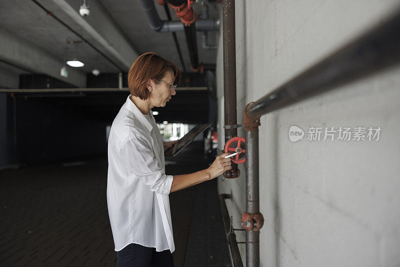 消防管道的检查和盘点。红发女子，理赔代理人在公寓停车场检查并登记灭火系统