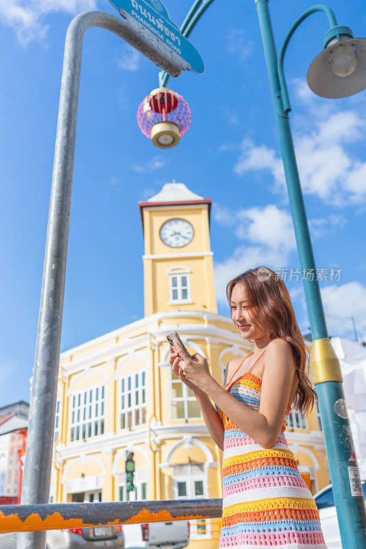 Z世代亚洲女性在旅行中使用智能手机探索普吉岛旧城的魅力，随时随地连接社交媒体。年轻女子与设备互动。通过设备连接生活方式。