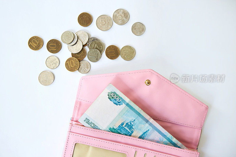 一张1000卢布的俄罗斯钞票放在一个粉红色的妇女钱包里，旁边是散落的各种面值的硬币。节约和节俭的观念。