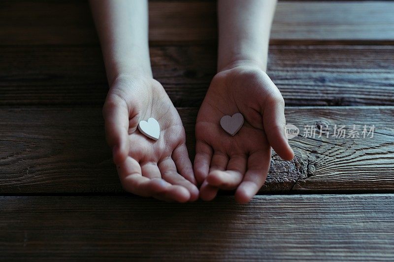 孩子手里拿着白色的心在木桌上。