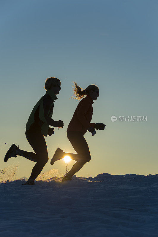 日落时分，一对年轻夫妇在雪地上奔跑