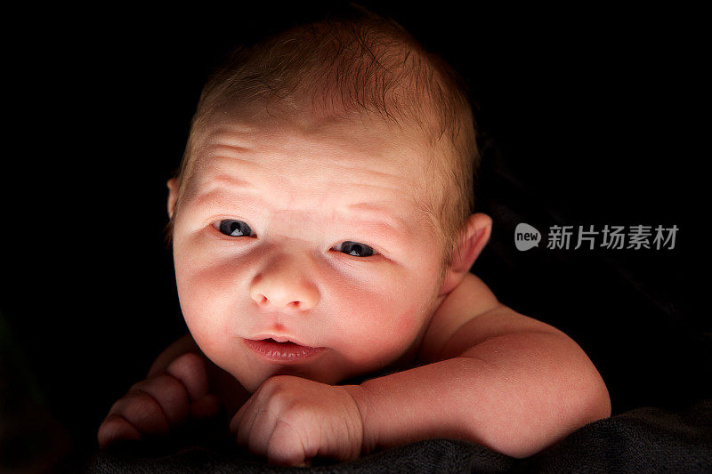 在黑色背景下睁开眼睛的新生男婴